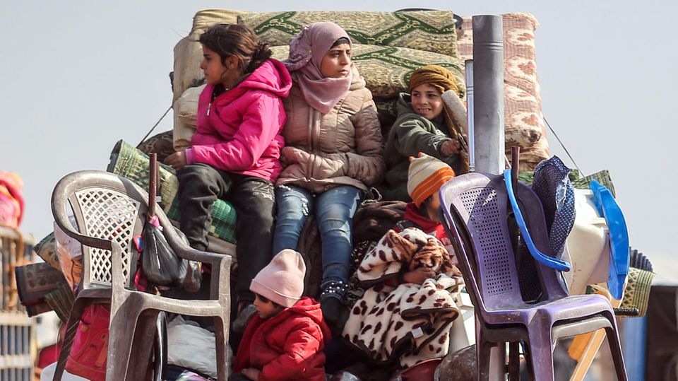 Kinder sitzen auf der Ladefläche eines Kleintransporters auf den Habseligkeiten ihrer Familie