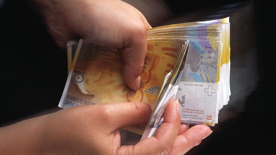 Eine Person hält ein Bündel Zehnernoten in Schweizer Franken in den Händen