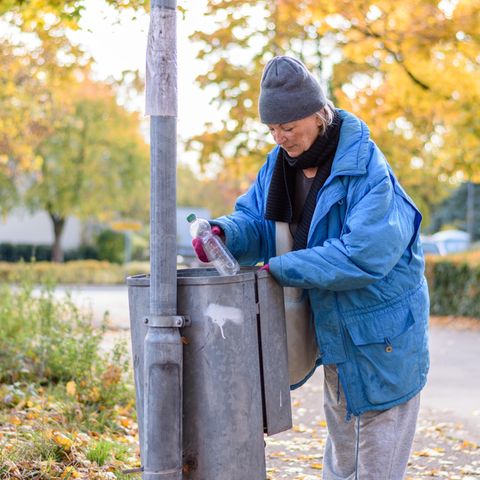 Eine Frau sucht in einem Mülleimer nach Pfandflaschen