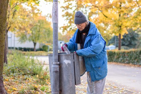 Eine Frau sucht in einem Mülleimer nach Pfandflaschen