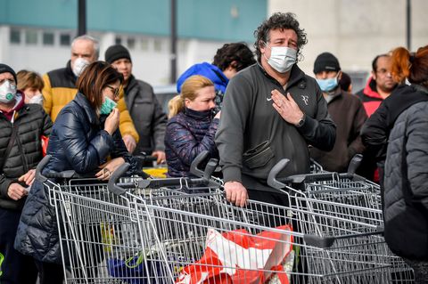 Menschen tragen Atemschutzmasken und stehen vor einem Supermarkt in einer Schlange