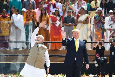 Auf einer Tribüne in einem Stadion stehen Narendra Modi und Donald Trump und winken Zuschauern zu