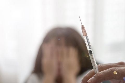 Eine Frau hält eine Spritze, im Hintergrund sieht man ein Mädchen