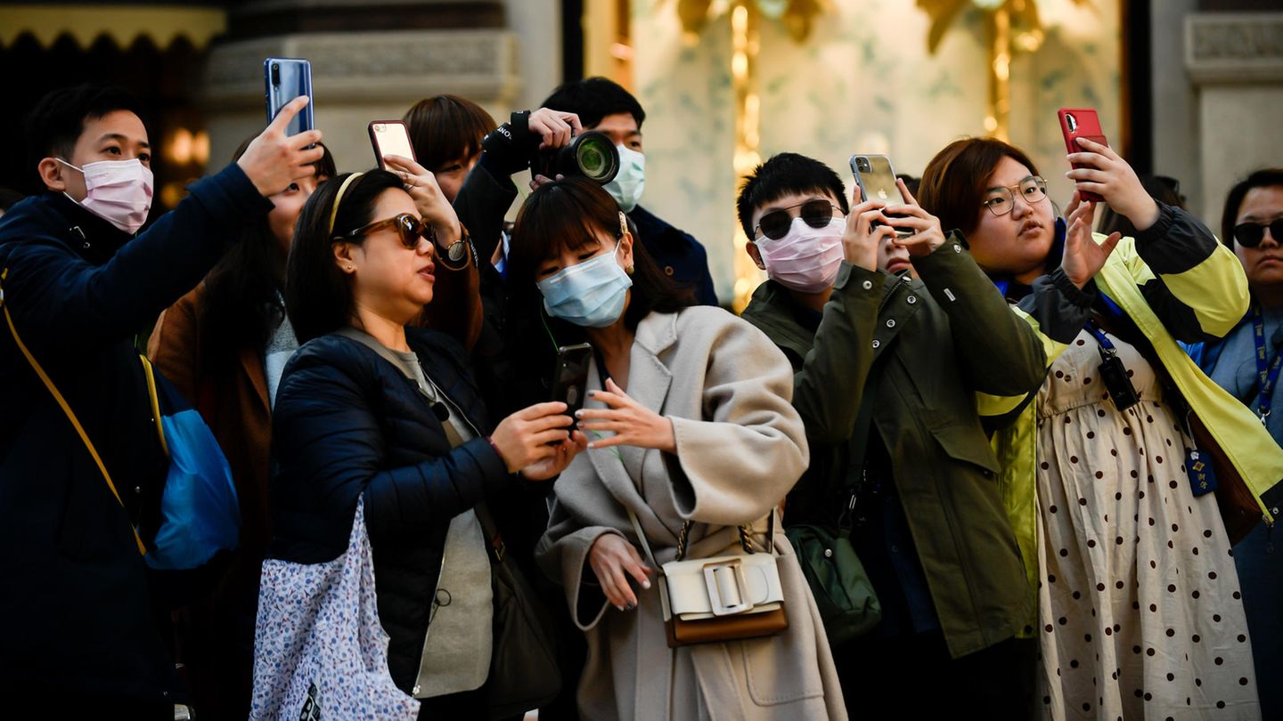 Touristen tragen Mundschutz und fotografieren mit ihren Smartphones
