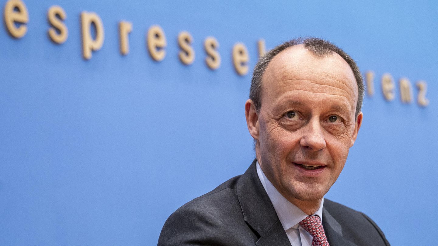 Vor einer blauen Wand mit "Bundespressekonferenz"-Schriftzug sitzt Friedrich Merz in einem Anzug und lächelt.