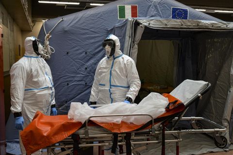 Turin: Zwei Mitarbeiter in Schutzanzügen stehen in einem Krankenhaus neben einer Liege