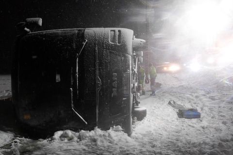 Auf einer verschneiten Autobahn liegt ein Reisebus im Dunkeln auf der rechten Seite