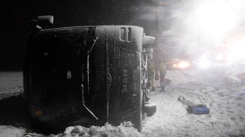 Auf einer verschneiten Autobahn liegt ein Reisebus im Dunkeln auf der rechten Seite