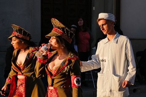 Zwei Frauen mit tiefen Ausschnitten gehen in SS-Uniformen vor einem Mann in KZ-Kleidung