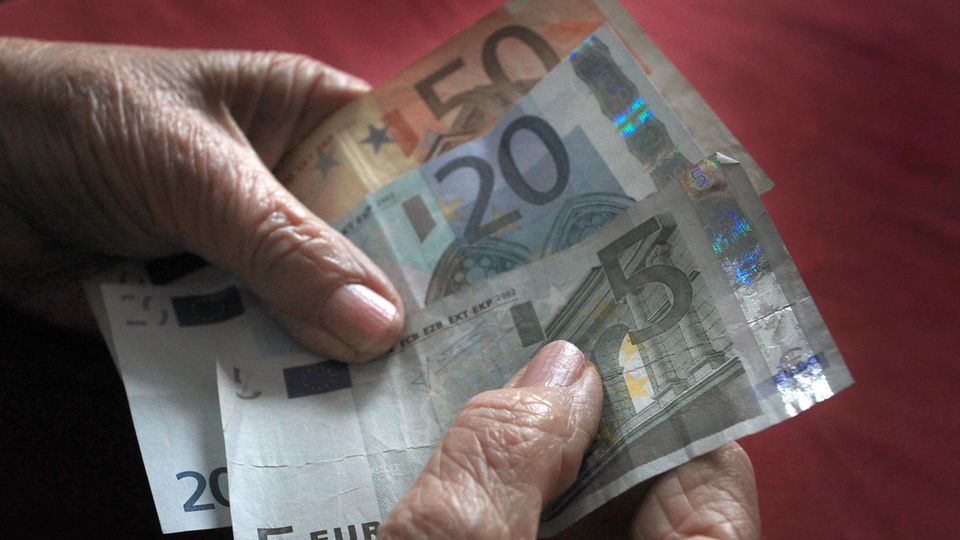 Die Hände einer alten Frau halten einen 50-, einen 20- und einen 5-Euro-Schein