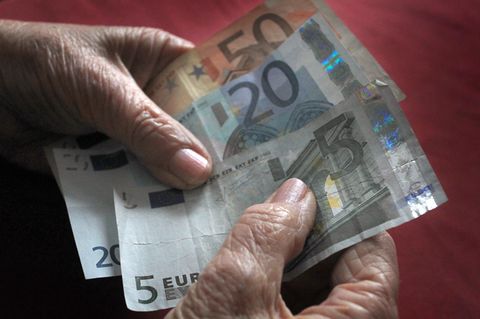 Die Hände einer alten Frau halten einen 50-, einen 20- und einen 5-Euro-Schein