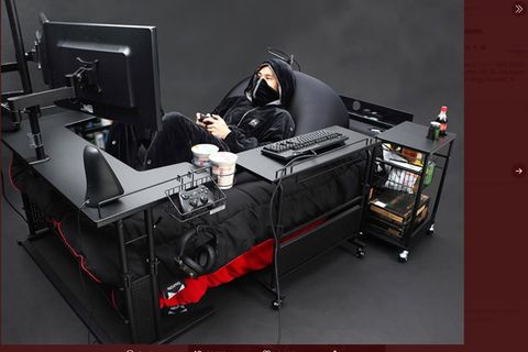 Ein junger Mann liegt in einem Bett, das mit Bildschirmen, Konsole und Tastatur ausgestattet ist