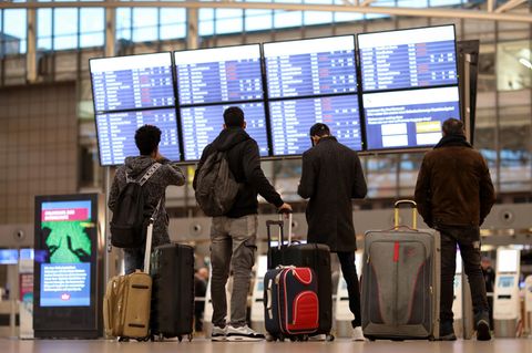 Ist mein Flug pünktlich? Passagiere stehen vor einer Anzeigetafel im Terminal eines Flughafens. 