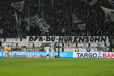 Am Zaun in einem Fußballstadion hängt ein weißes Banner mit schwarzer Schrift: "DFB Du Hurensohn"