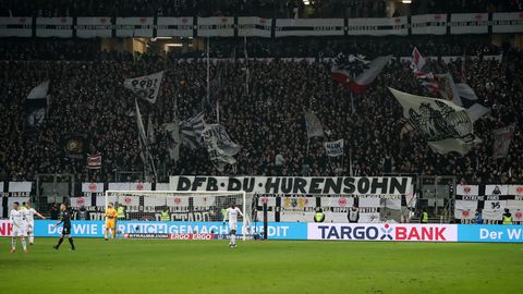 Am Zaun in einem Fußballstadion hängt ein weißes Banner mit schwarzer Schrift: "DFB Du Hurensohn"