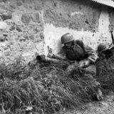 Deutsche Fallschirmspringer mit dem Panzerschreck in der Normandie. Der Schütze sucht die Deckung durch das Gebäude.