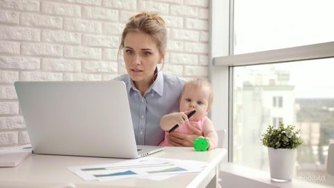 Eine Frau sitzt vor einem Laptop und hält gleichzeitig ein Baby im Arm