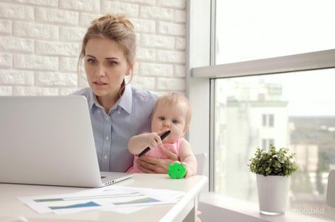 Eine Frau sitzt vor einem Laptop und hält gleichzeitig ein Baby im Arm