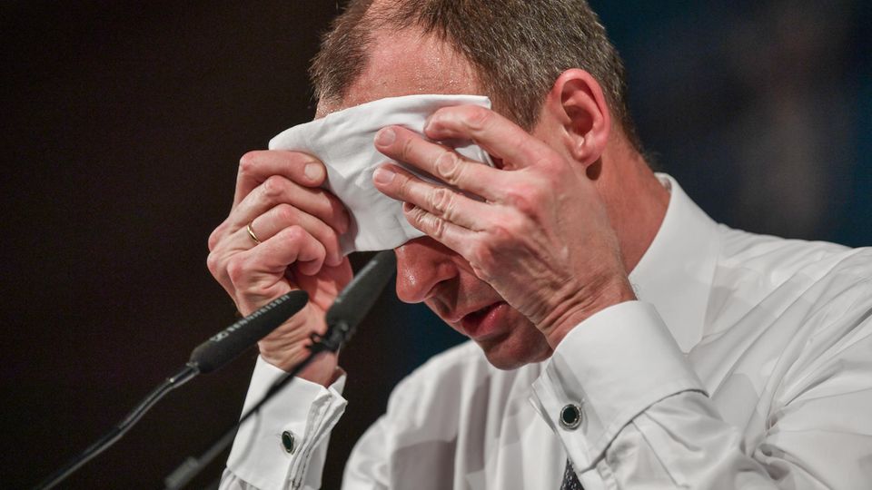 Friedrich Merz Friedrich Merz sitzt schwitzend vor zwei Mikrofonen und wischt sich mit einem weißen Tuch die Stirn