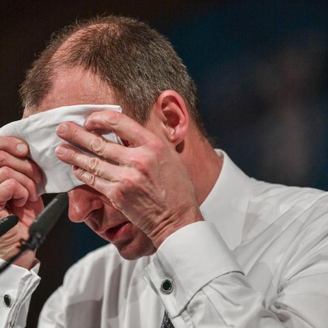 Friedrich Merz sitzt schwitzend vor zwei Mikrofonen und wischt sich mit einem weißen Tuch die Stirn