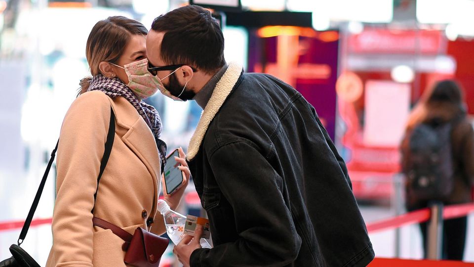 Ein Paar deutet Mundschutz tragend einen Kuss an