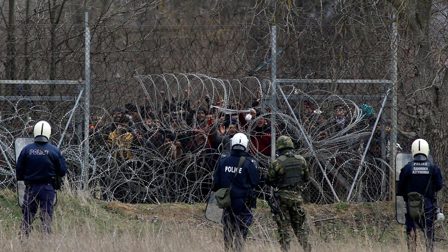 Flüchtlinge vor einem bewachten Stacheldrahtzaun