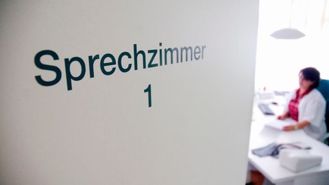 Tür eines Sprechzimmers. Dahinter sitzt eine Ärztin