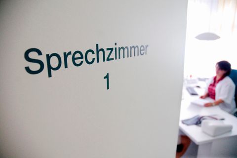 Tür eines Sprechzimmers. Dahinter sitzt eine Ärztin