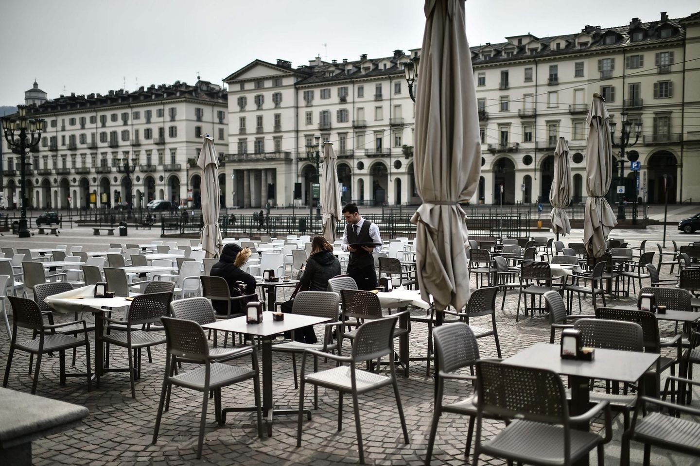 Zwei mutige Gäste auf einer verlassenen Caféterrasse auf der Piazza Vittorio in Turin. Bars und Restaurants können vorerst von 6 bis 18 Uhr geöffnet bleiben, sofern ein Sicherheitsabstand von mindestens einem Meter zwischen den Gästen eingehalten wird.