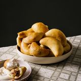 Piroggen      Zutaten:  250 g geräucherter Speck, in 1 cm große Würfel geschnitten 1 Msp. gemahlener Kardamom, 150 g Zwiebeln, fein gehackt, Pflanzenöl zum Braten (nach Belieben) 1 Ei, verquirlt, 50 ml Milch, saure Sahne zum Servieren (nach Belieben)      Teig:  280 ml Milch, 70 g Butter, 2 TL Zucker, Salz, 7 g Trockenhefe, 500 g Mehl, plus etwas mehr, 1 großes Ei, verquirlt      Zubereitung:  Speck, Kardamom und Zwiebeln in einer Pfanne bei mittlerer Hitze 10 Minuten braten, bis die Zwiebeln Fett aus dem Speck ausgelassen. (Bei magerem Speck muss eventuell etwas Pflanzenfett dazugegeben werden.) Beiseitestellen.  Für den Teig die Milch in einem Topf bei schwacher Hitze langsam erwärmen. Butter, Zucker und ½ TL Salz einrühren, den Topf vom Herd nehmen. Die Milchmischung in eine Schüssel gießen und auf Zimmertemperatur abkühlen lassen (das ist wichtig, weil zu große Wärme die Hefe tötet).  Hefe und Mehl in einer weiteren Schüssel vermischen, dann die abgekühlte Milchmischung unterrühren. Das Ei hinzufügen und mit den Händen alles zu einem Teig verkneten. Den Teig in einer Schüssel etwa 5 Minuten kneten, bis er weich und elastisch ist. Zu einer Kugel formen, wieder in die Schüssel legen und diese mit einem sauberen Küchentuch abdecken. Den Teig an einem warmen Ort etwa 1 Stunde gehen lassen, bis er etwa die doppelte Größe erreicht hat.  Den Teig auf einer bemehlten Arbeitsfläche etwas mehr als 5 mm dick ausrollen. Mit einem Trinkglas oder Keksausstecher Kreise mit einem Durchmesser von 7 cm ausstechen. Dabei Teigreste immer wieder zusammendrücken, um so viele Kreise wie möglich zu erhalten. In einen der Teigkreise 1 Teelöffel der Füllung geben und den Teig so zusammenfalten, dass eine Halbmondform entsteht. Den Rand zusammendrücken und unter die Pirogge klappen, dann die Pirogge auf das vorbereitete Backblech legen. Mit dem verbleibenden Teig und der restlichen Füllung ebenso verfahren. Zwischen den Piroggen auf dem Backblech 8 cm Platz lassen, dann an einem warmen Ort nochmals 15 Minuten gehen lassen. Den Backofen auf 190 °C vorheizen und ein Backblech mit Backpapier auslegen. Ei und Milch in einer Schüssel vermischen und damit großzügig die Oberfläche der Piroggen bestreichen. Etwa 10 Minuten backen, bis die Teigtaschen goldbraun sind. Warm servieren, nach Belieben mit saurer Sahne.