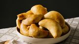 Piroggen      Zutaten:  250 g geräucherter Speck, in 1 cm große Würfel geschnitten 1 Msp. gemahlener Kardamom, 150 g Zwiebeln, fein gehackt, Pflanzenöl zum Braten (nach Belieben) 1 Ei, verquirlt, 50 ml Milch, saure Sahne zum Servieren (nach Belieben)      Teig:  280 ml Milch, 70 g Butter, 2 TL Zucker, Salz, 7 g Trockenhefe, 500 g Mehl, plus etwas mehr, 1 großes Ei, verquirlt      Zubereitung:  Speck, Kardamom und Zwiebeln in einer Pfanne bei mittlerer Hitze 10 Minuten braten, bis die Zwiebeln Fett aus dem Speck ausgelassen. (Bei magerem Speck muss eventuell etwas Pflanzenfett dazugegeben werden.) Beiseitestellen.  Für den Teig die Milch in einem Topf bei schwacher Hitze langsam erwärmen. Butter, Zucker und ½ TL Salz einrühren, den Topf vom Herd nehmen. Die Milchmischung in eine Schüssel gießen und auf Zimmertemperatur abkühlen lassen (das ist wichtig, weil zu große Wärme die Hefe tötet).  Hefe und Mehl in einer weiteren Schüssel vermischen, dann die abgekühlte Milchmischung unterrühren. Das Ei hinzufügen und mit den Händen alles zu einem Teig verkneten. Den Teig in einer Schüssel etwa 5 Minuten kneten, bis er weich und elastisch ist. Zu einer Kugel formen, wieder in die Schüssel legen und diese mit einem sauberen Küchentuch abdecken. Den Teig an einem warmen Ort etwa 1 Stunde gehen lassen, bis er etwa die doppelte Größe erreicht hat.  Den Teig auf einer bemehlten Arbeitsfläche etwas mehr als 5 mm dick ausrollen. Mit einem Trinkglas oder Keksausstecher Kreise mit einem Durchmesser von 7 cm ausstechen. Dabei Teigreste immer wieder zusammendrücken, um so viele Kreise wie möglich zu erhalten. In einen der Teigkreise 1 Teelöffel der Füllung geben und den Teig so zusammenfalten, dass eine Halbmondform entsteht. Den Rand zusammendrücken und unter die Pirogge klappen, dann die Pirogge auf das vorbereitete Backblech legen. Mit dem verbleibenden Teig und der restlichen Füllung ebenso verfahren. Zwischen den Piroggen auf dem Backblech 8 cm Platz lassen, dann an einem warmen Ort nochmals 15 Minuten gehen lassen. Den Backofen auf 190 °C vorheizen und ein Backblech mit Backpapier auslegen. Ei und Milch in einer Schüssel vermischen und damit großzügig die Oberfläche der Piroggen bestreichen. Etwa 10 Minuten backen, bis die Teigtaschen goldbraun sind. Warm servieren, nach Belieben mit saurer Sahne.