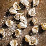 Pelmeni      Zutaten:      Teig:  300 g Mehl, plus mehr zum Verarbeiten ,1 kleines Ei, 35 g Butter, in 2 cm große Würfel geschnitten, Salz      Füllung:  250 g Schweinehackfleisch, 250 g Rinderhackfleisch, 1 kleine Zwiebel, fein gerieben, Salz gemahlener schwarzer Pfeffer      Zum Servieren:  500 ml Hühnerbrühe (oder Gemüsebrühe), Salz, 100 g Speck, fein gewürfelt und kross gebraten, 2 EL gehackter Schnittlauch, 1 EL gehackter Dill, 150 g saure Sahne      Zubereitung:  Für den Teig Mehl, Ei, Butter und 1/2 TL in einer Salz Küchenmaschine zu einem seidigen, weichen Teig kneten. Den Teig in eine Schüssel legen, mit einem Küchentuch abdecken und mindestens 30 Minuten ruhen lassen.  Für die Füllung Fleisch, Zwiebel, 1 TL Salz und 1 TL Pfeffer in einer Schüssel mit den Händen gut vermischen.  Den Teig in vier gleich große Stücke teilen. Ein stück auf einer bemehlten Arbeitsfläche etwa 5 mm dick ausrollen. Mit einem Trinkglas Kreise mit einem Durchmesser von 8 cm ausstechen. Die Teigreste immer wieder zusammenlegen und ausrollen, um so viele Kreise wie möglich zu erhalten.  In die Mitte eines Kreises 1 TL Füllung geben, dann den Kreis zusammenklappen, sodass eine Halbmondform entsteht. Den aufeinandergelegten Rand gut zusammendrücken, dann die Spitzen so zueinanderklappen, dass sie aufeinanderliegen. Wieder gut zusammendrücken. Pelmeni auf ein bemehltes Tablett legen und nun mit allen Kreisen ebenso verfahren.  Zum Servieren die Hühner- oder Gemüsebrühe in einem Topf erwärmen und in einem anderen großen Topf Salzwasser zum Kochen bringen. Die Pelmeni vorsichtig in das kochende Wasser gleiten lassen und 5–7 Minuten kochen, bis sie an die Oberfläche steigen. Dann mit einem Schaumlöffel aus dem Wasser heben und auf Schalen verteilen. Die warme Brühe darübergeben und mit dem knusprigen Speck, Schnittlauch, Dill und großen Klecksen saurer Sahne garnieren.