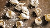 Pelmeni      Zutaten:      Teig:  300 g Mehl, plus mehr zum Verarbeiten ,1 kleines Ei, 35 g Butter, in 2 cm große Würfel geschnitten, Salz      Füllung:  250 g Schweinehackfleisch, 250 g Rinderhackfleisch, 1 kleine Zwiebel, fein gerieben, Salz gemahlener schwarzer Pfeffer      Zum Servieren:  500 ml Hühnerbrühe (oder Gemüsebrühe), Salz, 100 g Speck, fein gewürfelt und kross gebraten, 2 EL gehackter Schnittlauch, 1 EL gehackter Dill, 150 g saure Sahne      Zubereitung:  Für den Teig Mehl, Ei, Butter und 1/2 TL in einer Salz Küchenmaschine zu einem seidigen, weichen Teig kneten. Den Teig in eine Schüssel legen, mit einem Küchentuch abdecken und mindestens 30 Minuten ruhen lassen.  Für die Füllung Fleisch, Zwiebel, 1 TL Salz und 1 TL Pfeffer in einer Schüssel mit den Händen gut vermischen.  Den Teig in vier gleich große Stücke teilen. Ein stück auf einer bemehlten Arbeitsfläche etwa 5 mm dick ausrollen. Mit einem Trinkglas Kreise mit einem Durchmesser von 8 cm ausstechen. Die Teigreste immer wieder zusammenlegen und ausrollen, um so viele Kreise wie möglich zu erhalten.  In die Mitte eines Kreises 1 TL Füllung geben, dann den Kreis zusammenklappen, sodass eine Halbmondform entsteht. Den aufeinandergelegten Rand gut zusammendrücken, dann die Spitzen so zueinanderklappen, dass sie aufeinanderliegen. Wieder gut zusammendrücken. Pelmeni auf ein bemehltes Tablett legen und nun mit allen Kreisen ebenso verfahren.  Zum Servieren die Hühner- oder Gemüsebrühe in einem Topf erwärmen und in einem anderen großen Topf Salzwasser zum Kochen bringen. Die Pelmeni vorsichtig in das kochende Wasser gleiten lassen und 5–7 Minuten kochen, bis sie an die Oberfläche steigen. Dann mit einem Schaumlöffel aus dem Wasser heben und auf Schalen verteilen. Die warme Brühe darübergeben und mit dem knusprigen Speck, Schnittlauch, Dill und großen Klecksen saurer Sahne garnieren.