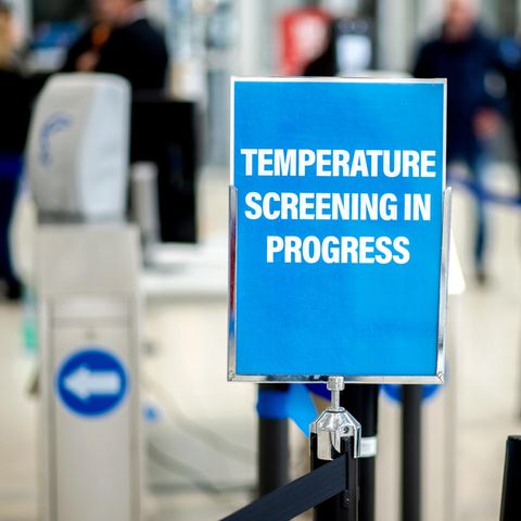 Ein Schild mit der Aufschrift "Temperature Screening in Progress" weist auf eine Einrichtung zur Messung der Körpertemperatur hin.