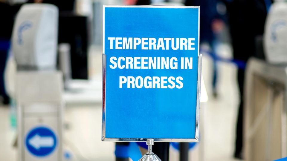 Ein Schild mit der Aufschrift "Temperature Screening in Progress" weist auf eine Einrichtung zur Messung der Körpertemperatur hin.