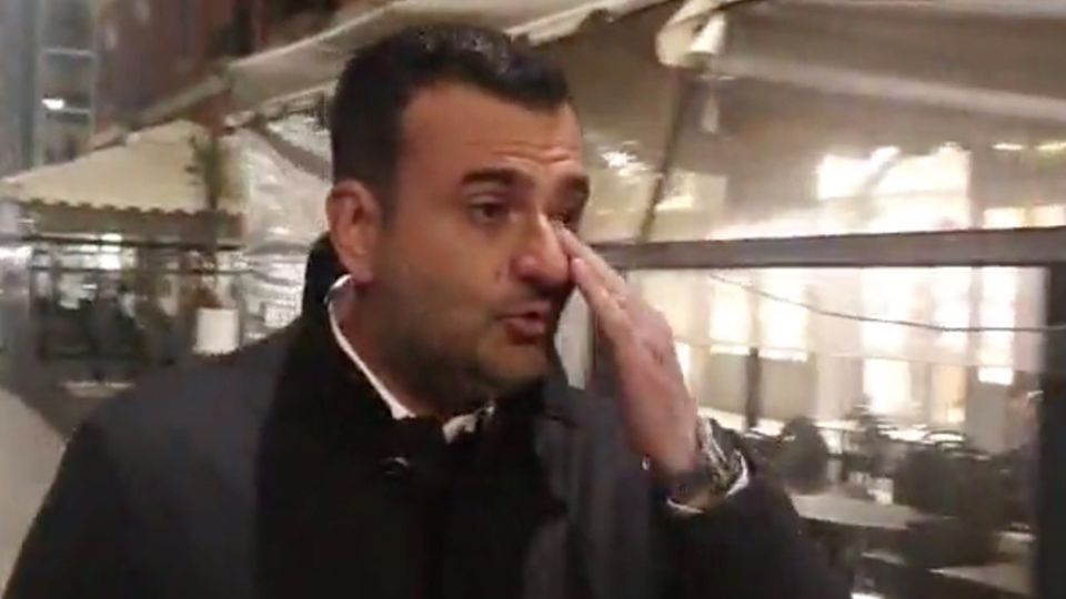 Ein eleganz gekleideter Mann mit schwarzen Locken wischt sich mit Links eine Träne aus dem Auge. Im Hintergrund ein Restaurant