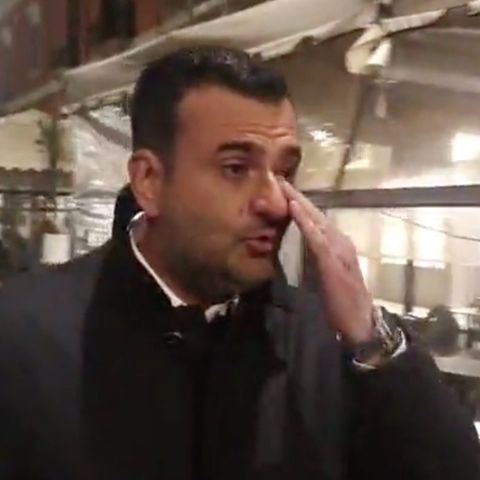 Ein eleganz gekleideter Mann mit schwarzen Locken wischt sich mit Links eine Träne aus dem Auge. Im Hintergrund ein Restaurant