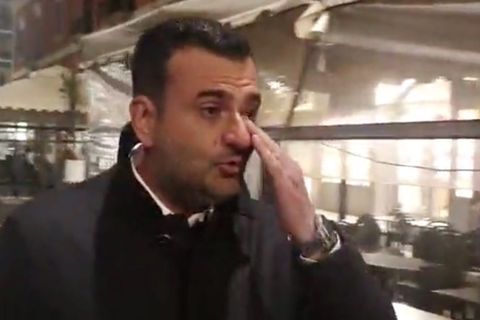 Ein eleganz gekleideter Mann mit schwarzen Locken wischt sich mit Links eine Träne aus dem Auge. Im Hintergrund ein Restaurant