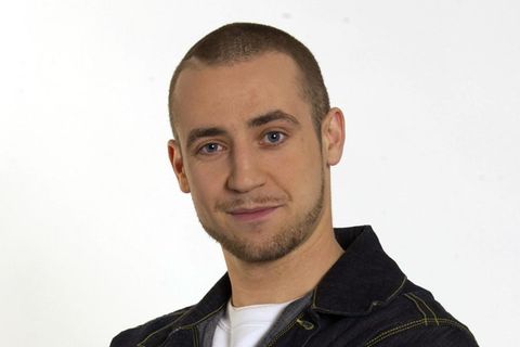 Ein junger Mann mit kurz rasierten Haaren und Drei-Tage-Bart steht mit verschränkten Armen da.