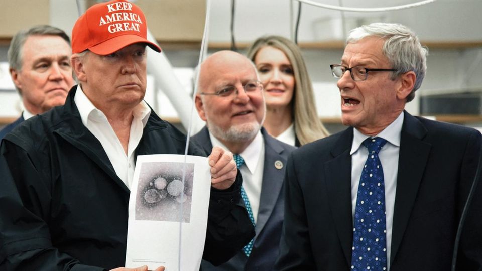 Donald Trump hält ein Bild des Virus in die Kamera