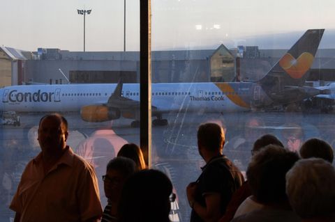 Passagiere schauen auf das Rollfeld, wo ein Flugzeug steht