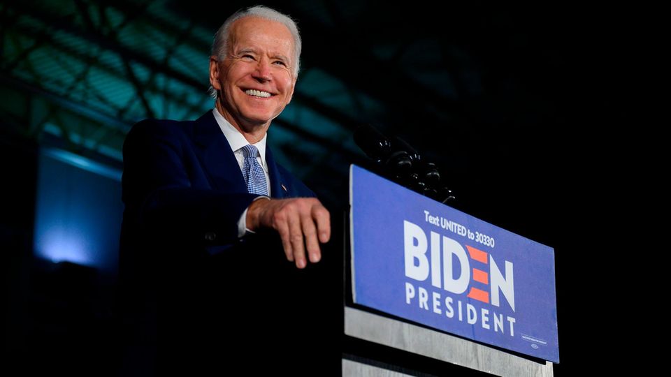 Joe Biden spricht von einem Podium und lächelt