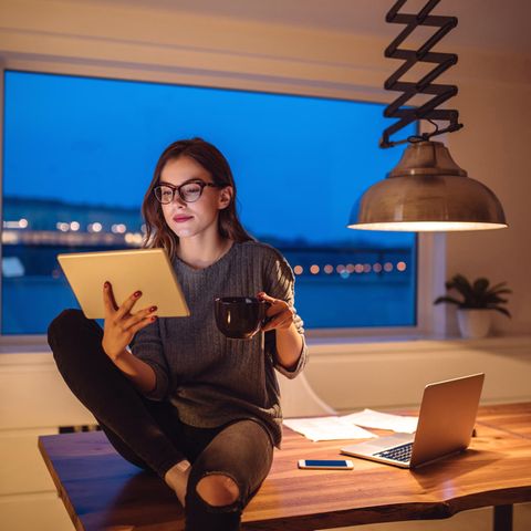 Eine junge Frau sitzt im Home Office und schaut auf ihr iPad