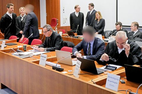 Die Angeklagten (3.v.l, und 2.v.r) stehen bzw. sitzen zusammen mit ihren Verteidigern im Landgericht auf der Anklagebank