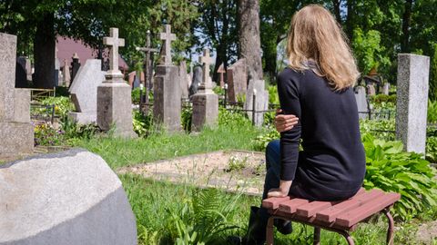 Eine junge Frau sitzt allein vor Grabsteinen
