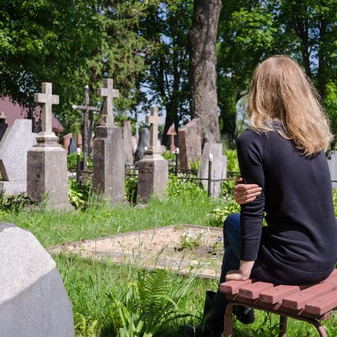 Eine junge Frau sitzt allein vor Grabsteinen