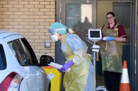 Eine Krankenschwester steht in Schutzkleidung neben einem Auto