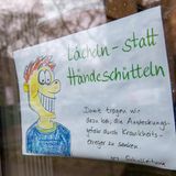 Dieses Schild mit dem Satz "Lächeln statt Händeschütteln" hängt an der Tür einer Grundschule in München