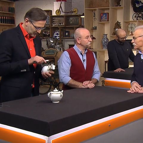 "Bares für Rares"-Experte Detlev Kümmel untersucht die Milchkanne, Moderator Horst Lichter lässt sich von Verkäufer Uwe Fischer die Herkunft der beiden Stücke erklären.