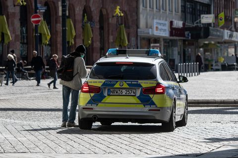 Ein Mann mit einem Mundschutz unterhält sich in der Fußgängerzone mit den Polizisten in einem Streifenwagen